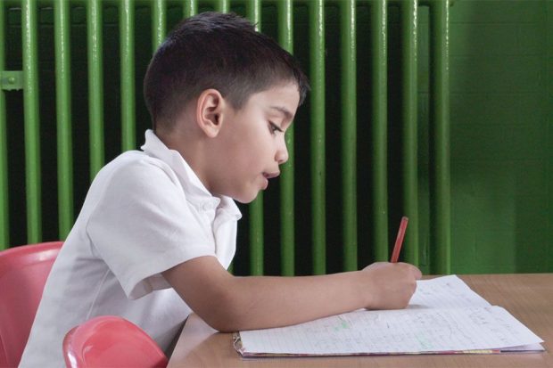 child filling in work pages with pen in a classroom