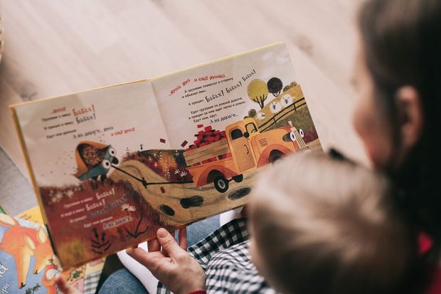 A child and parent reading a children's book with colourful pictures and text